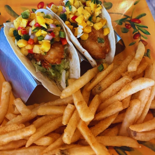 Two fish tacos with mango salsa and a side of french fries on a decorative orange plate.