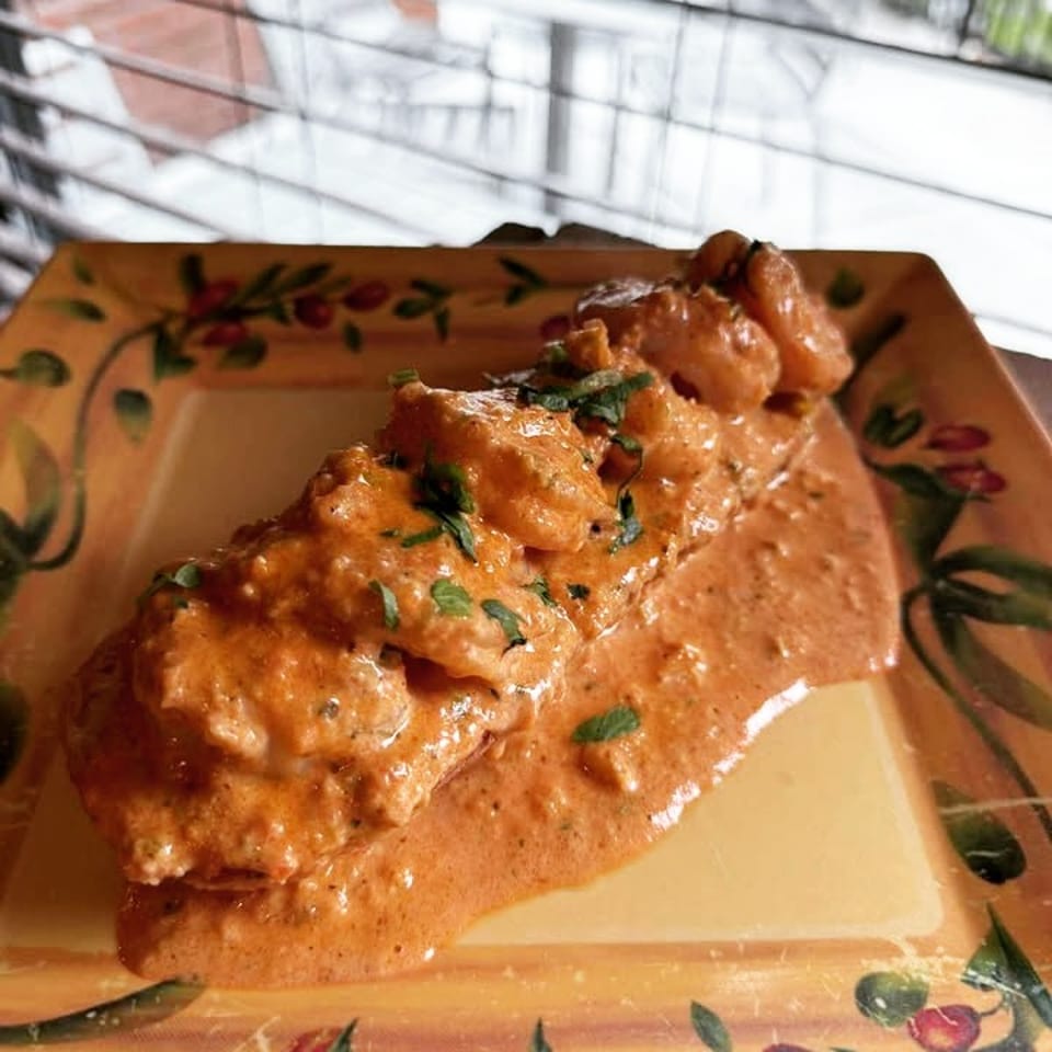 Creamy orange shrimp dish garnished with green herbs on a decorative plate.