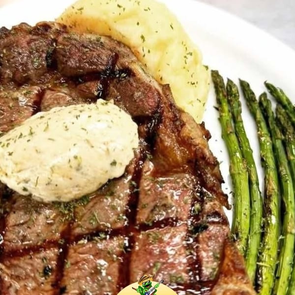Grilled steak with a dollop of butter, mashed potatoes, and asparagus on a white plate.