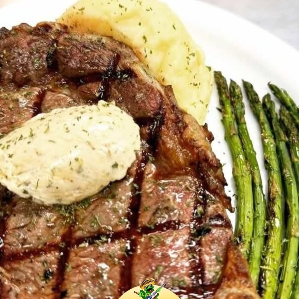 Grilled steak with a dollop of butter, mashed potatoes, and asparagus on a white plate.