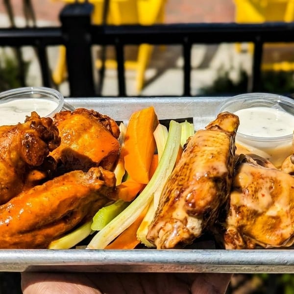 A metal tray of buffalo wings, carrots, celery, and dipping sauces, held outdoors.