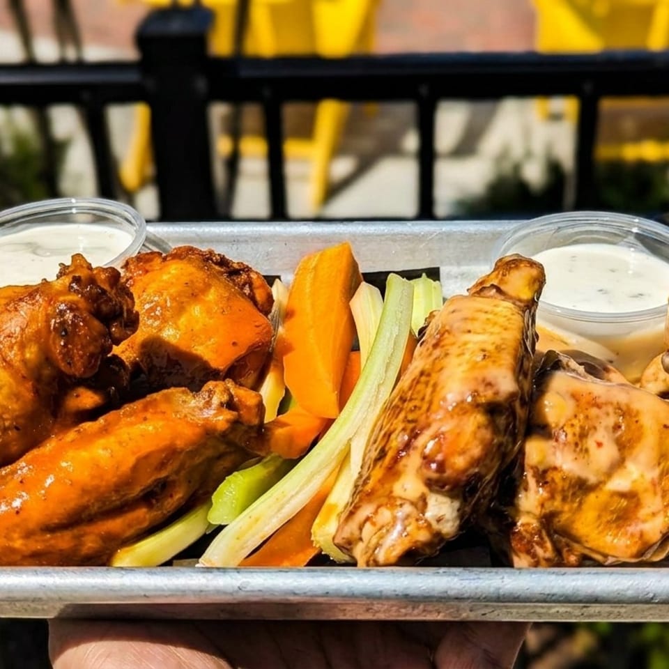 A metal tray of buffalo wings, carrots, celery, and dipping sauces, held outdoors.